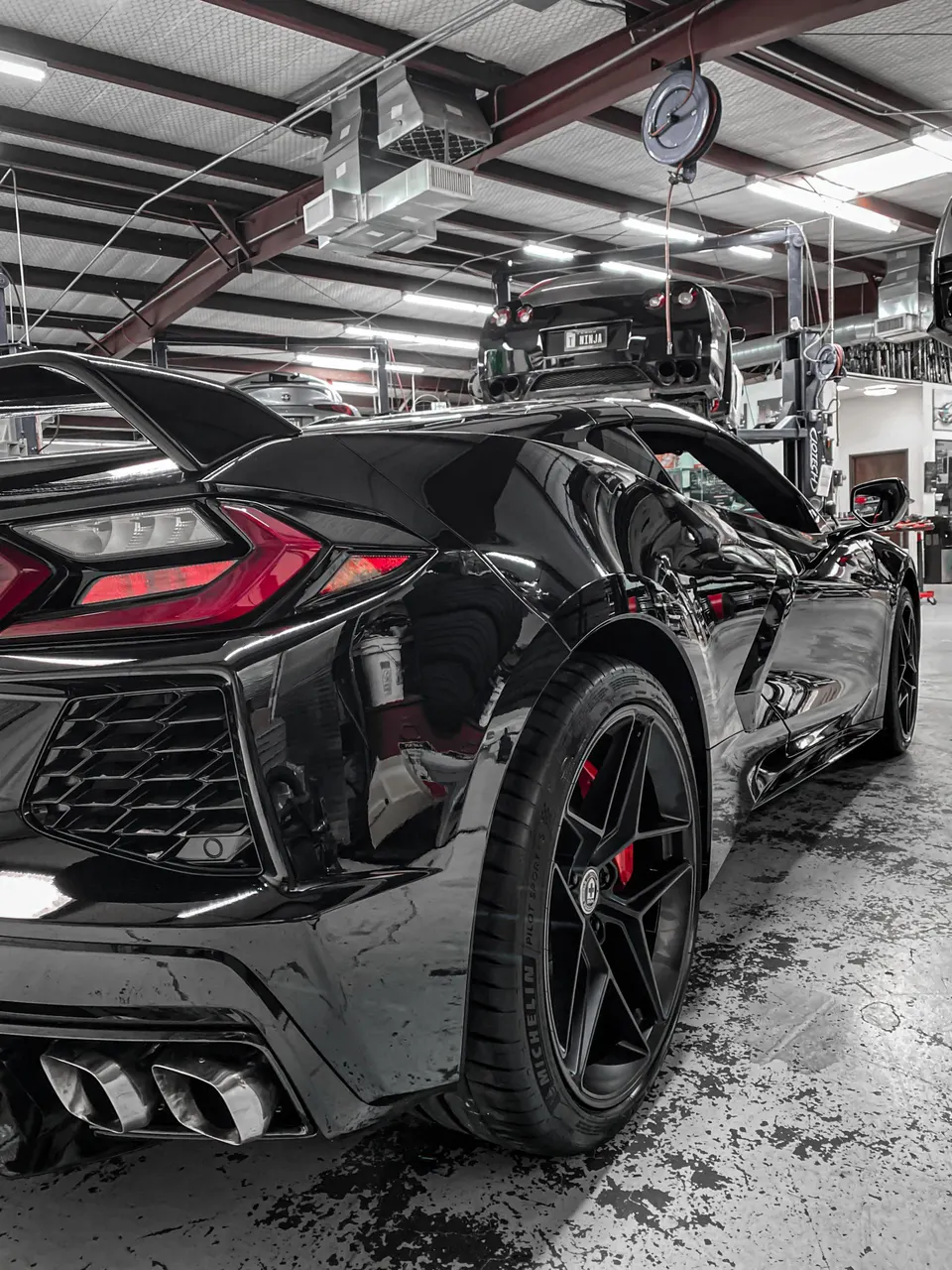 Black C8 Corvette with HRE wheels and quad exhaust tips in a performance tuning shop.