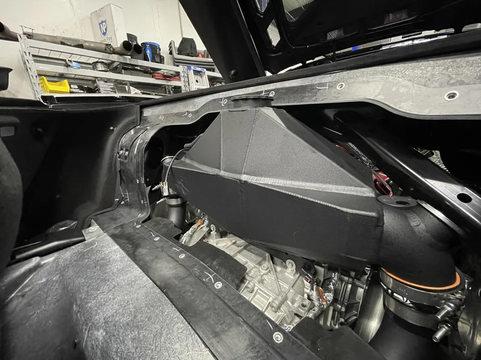 Close-up of a custom intake system and boost piping being installed in a high-performance car's engine bay at a tuning shop.