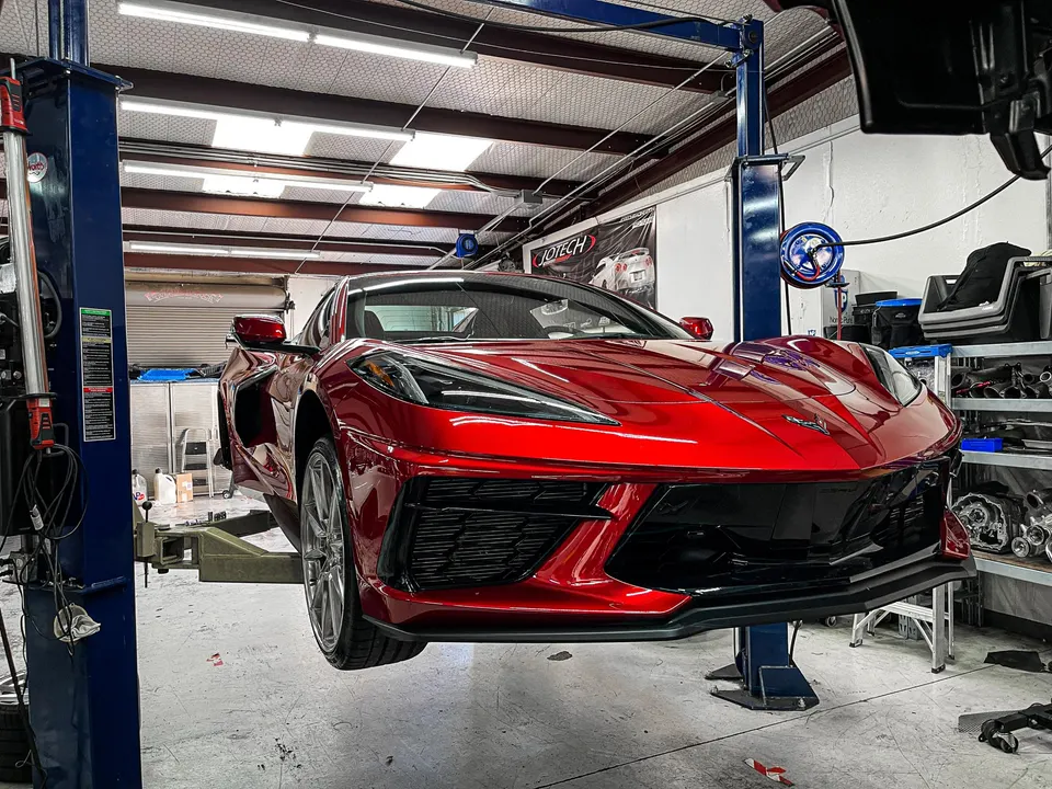 Red C8 Corvette on a car lift in a performance tuning shop, ready for service or modifications
