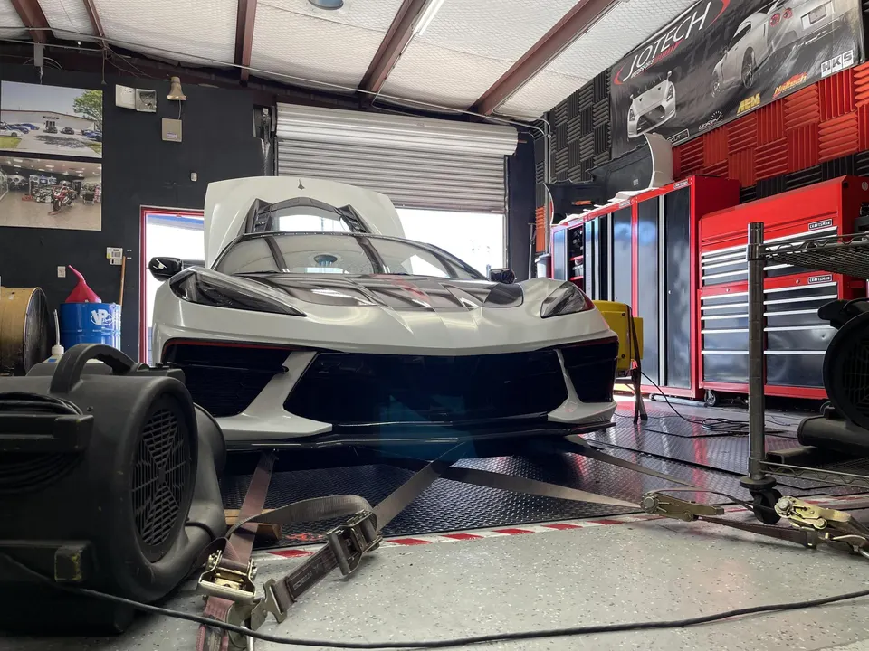White C8 Corvette strapped to a dynamometer in a performance tuning shop, ready for a dyno run.