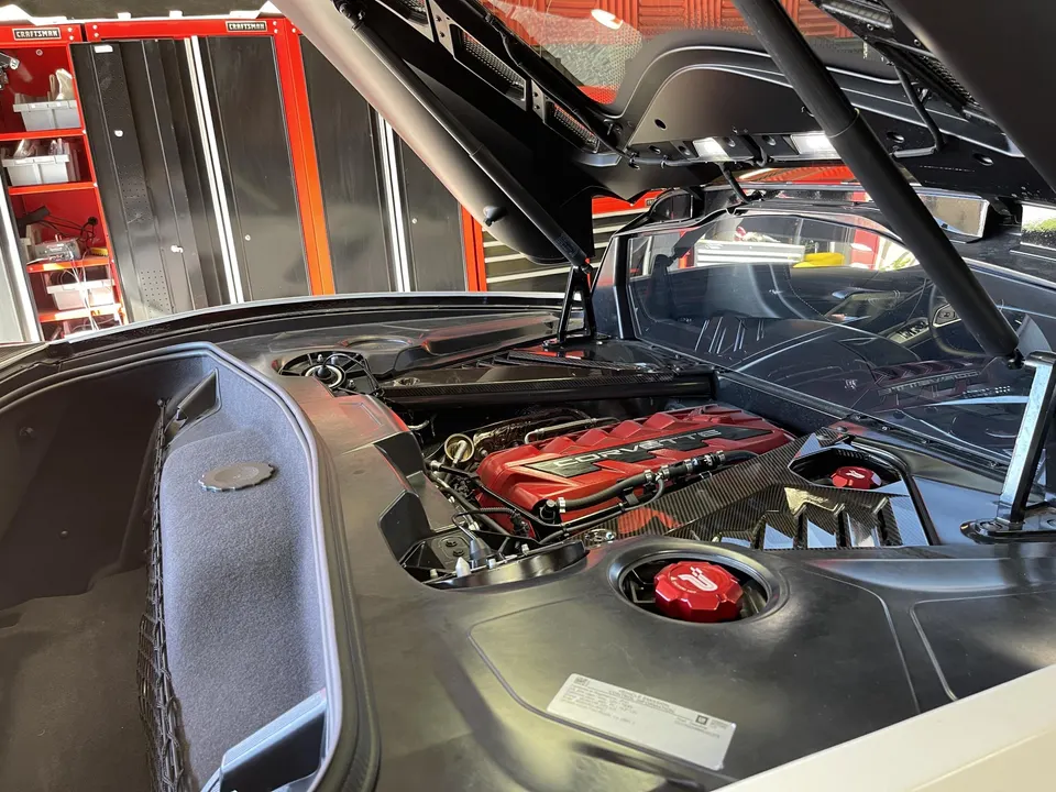 Close-up of a red Corvette C8 engine bay with carbon fiber accents in a shop setting.