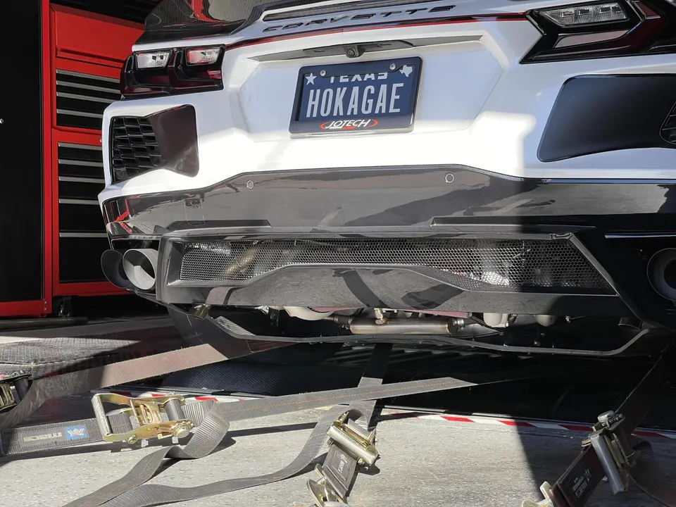 White C8 Corvette strapped to a dyno, showcasing its rear diffuser and aftermarket exhaust system.