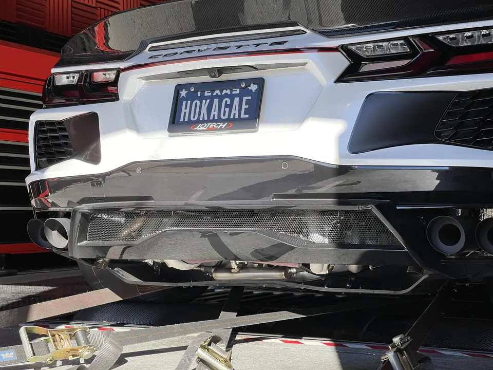 Rear view of a white Corvette C8 strapped on a dyno, featuring a custom exhaust system and carbon fiber diffuser.