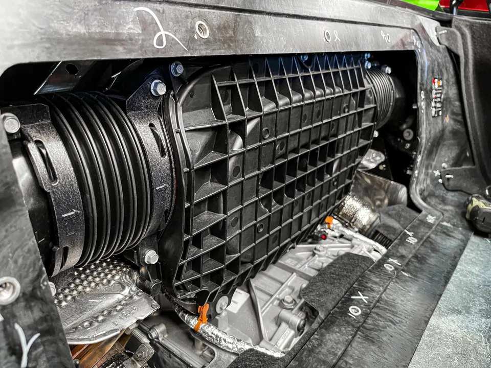 Close-up view of a car's induction system, featuring a black plastic airbox and ribbed intake hose in the engine bay.