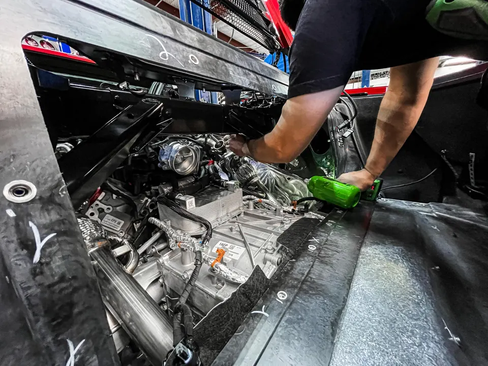 A mechanic working on the engine bay of a C8 Corvette, focusing on the throttle body and intake system during an install.