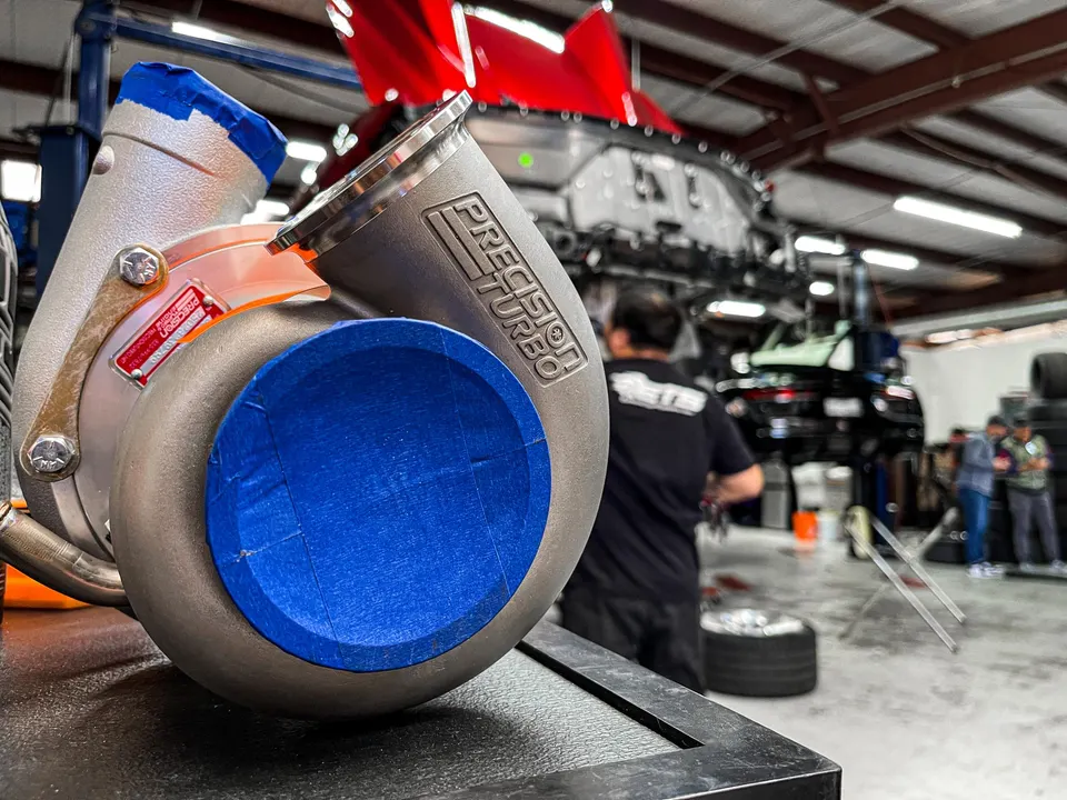 Close-up of a Precision Turbo turbocharger on a workbench in a performance tuning shop.