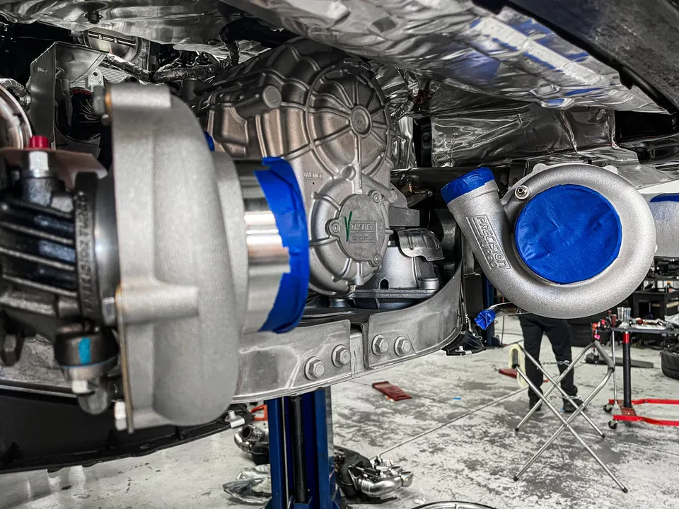Twin Precision Turbochargers being installed on the underside of a high-performance car in a shop