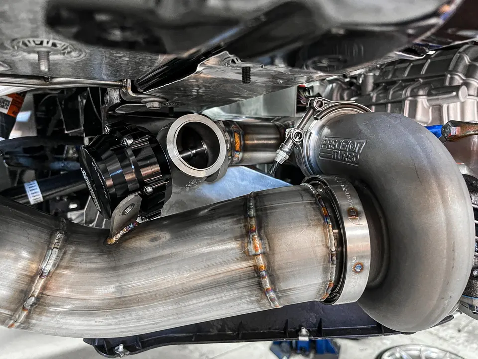 Close-up of a Precision Turbo turbocharger and wastegate installed with custom exhaust piping on a performance car.