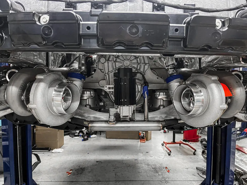 Twin turbochargers installed on the underside of a performance car on a lift at a tuning shop.