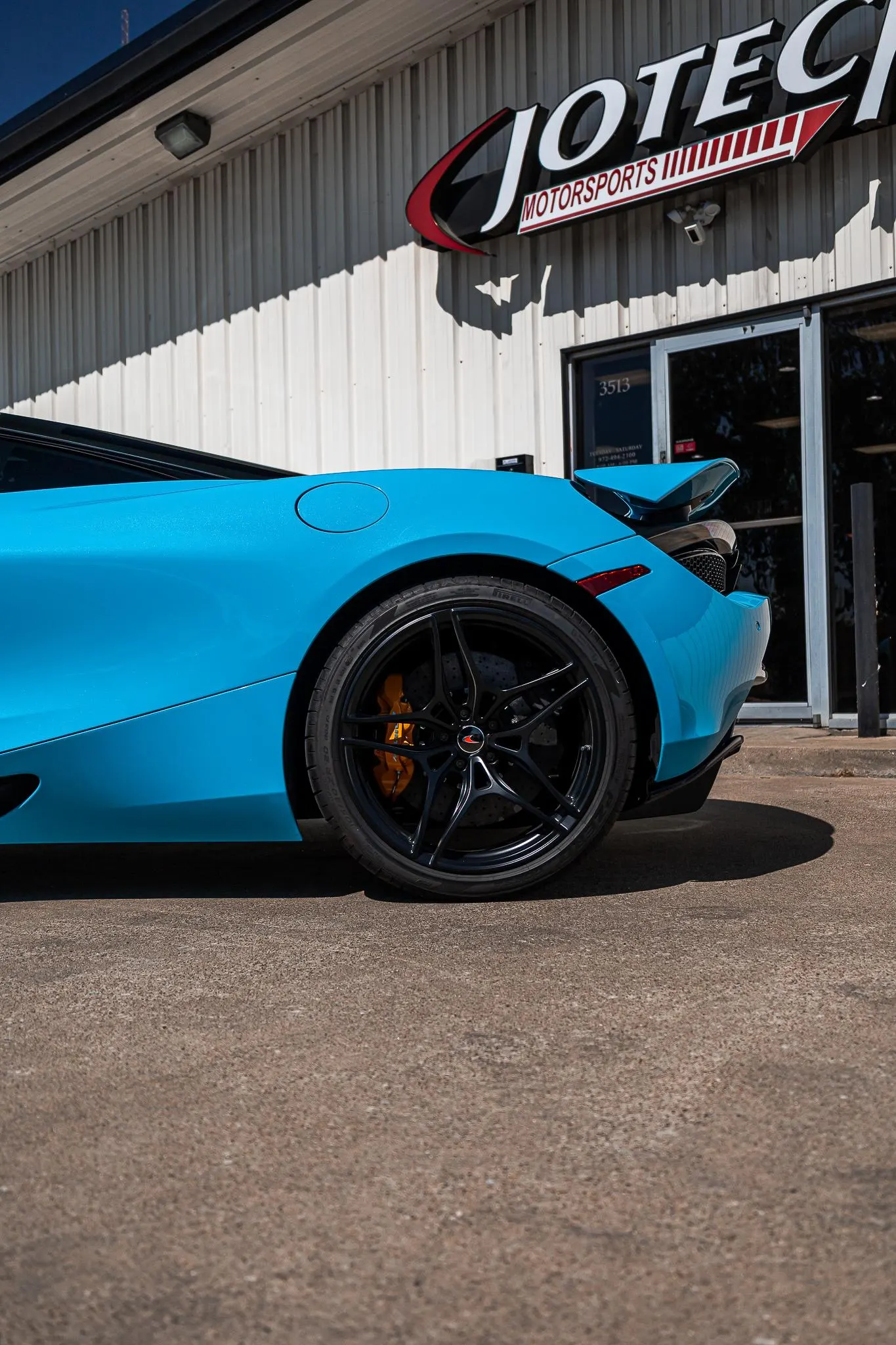 Blue McLaren supercar with black wheels and orange brake calipers parked outside Jotech Motorsports performance shop.