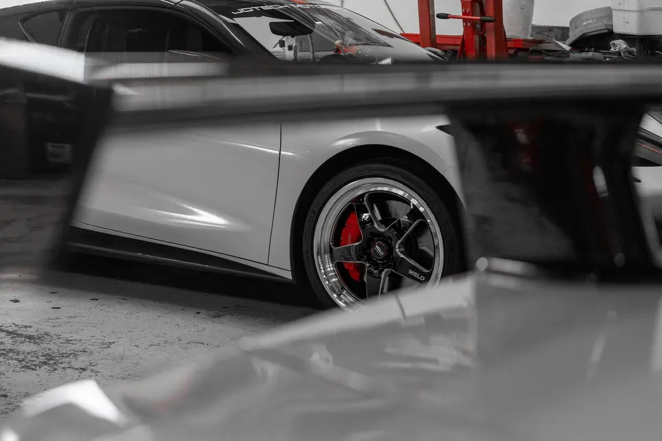 Close-up of a white sports car's black Weld wheel with a polished lip and red brake caliper in a shop.