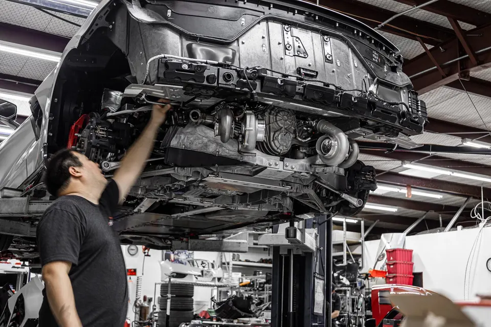 A mechanic works on the twin-turbo system of a car lifted in a performance tuning shop.