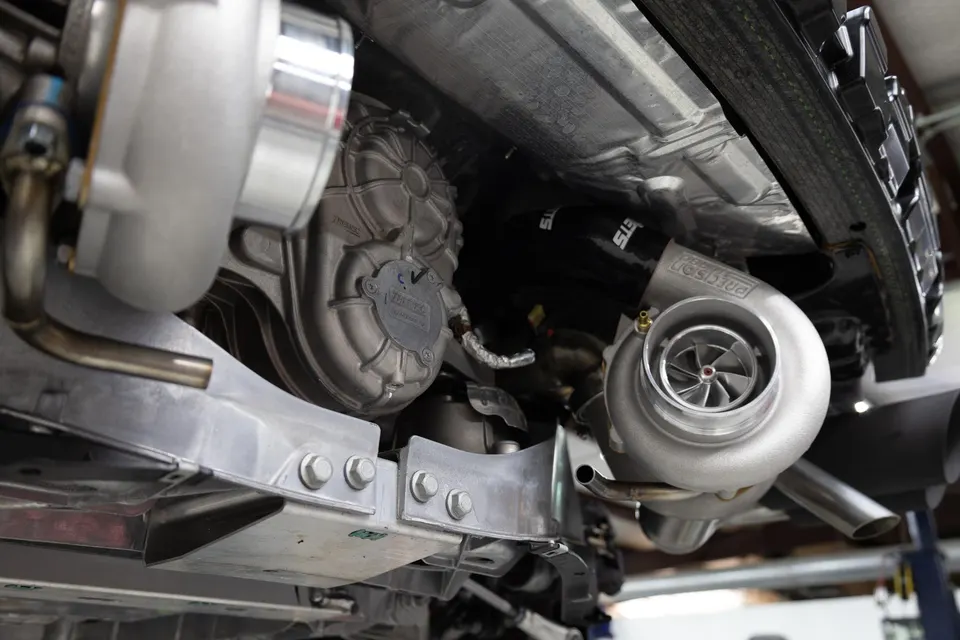 Underside view of a high-performance car showcasing twin turbochargers and custom exhaust system in a shop.