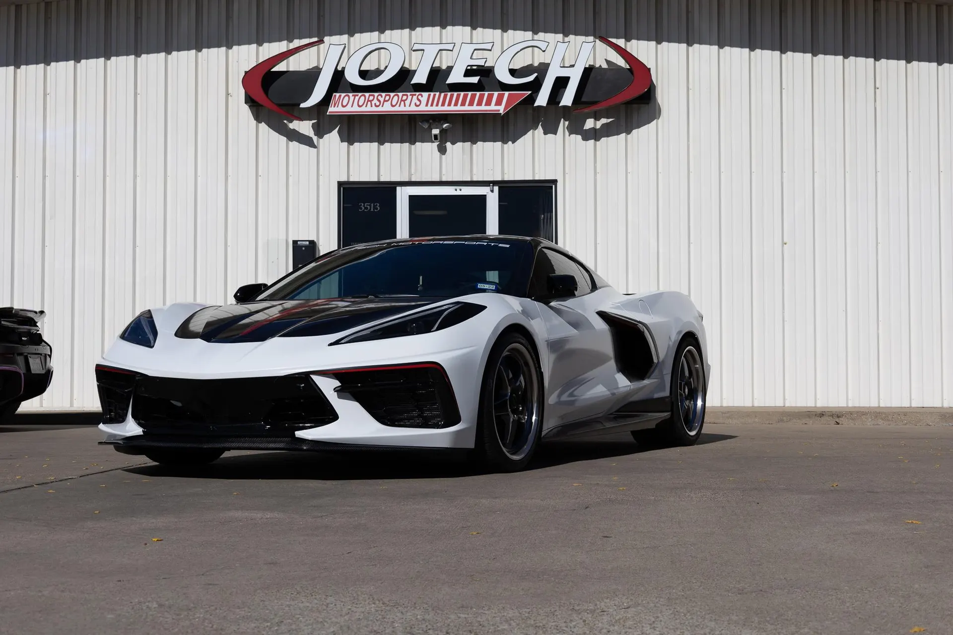 White Corvette C8 with black hood and custom wheels parked outside the Jotech Motorsports shop.