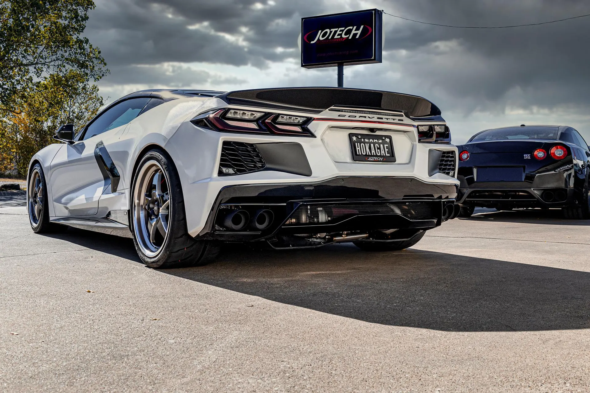White Corvette C8 with a carbon fiber wing and custom exhaust system parked next to a black Nissan GT-R at Jotech Motorsports.