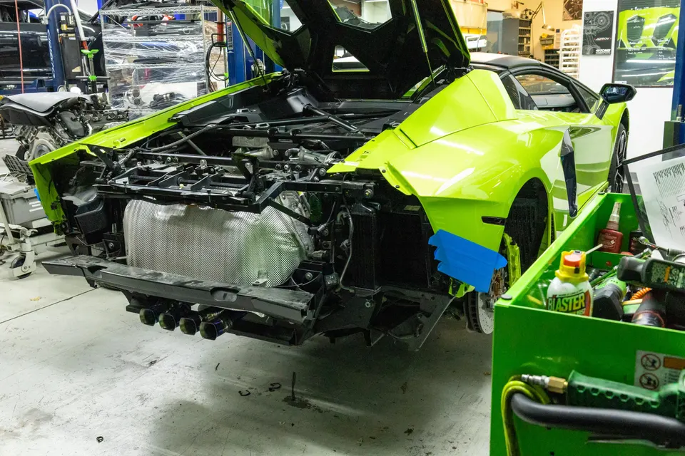 A lime green Lamborghini Aventador in a shop with its rear bumper removed, revealing the exhaust system during a build or repair.