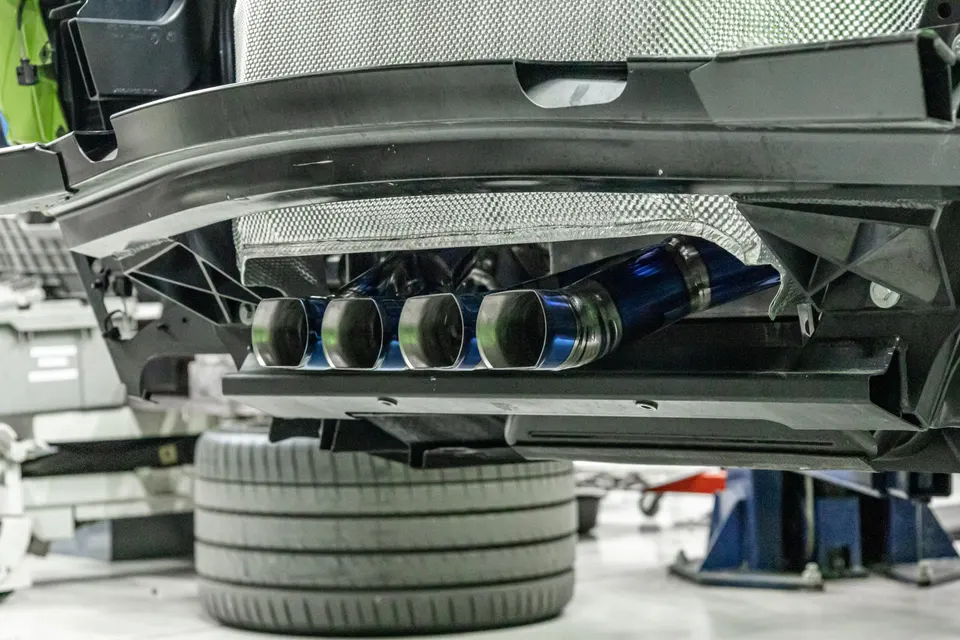 Close-up of a performance exhaust system with blue titanium tips on a car in a shop environment.