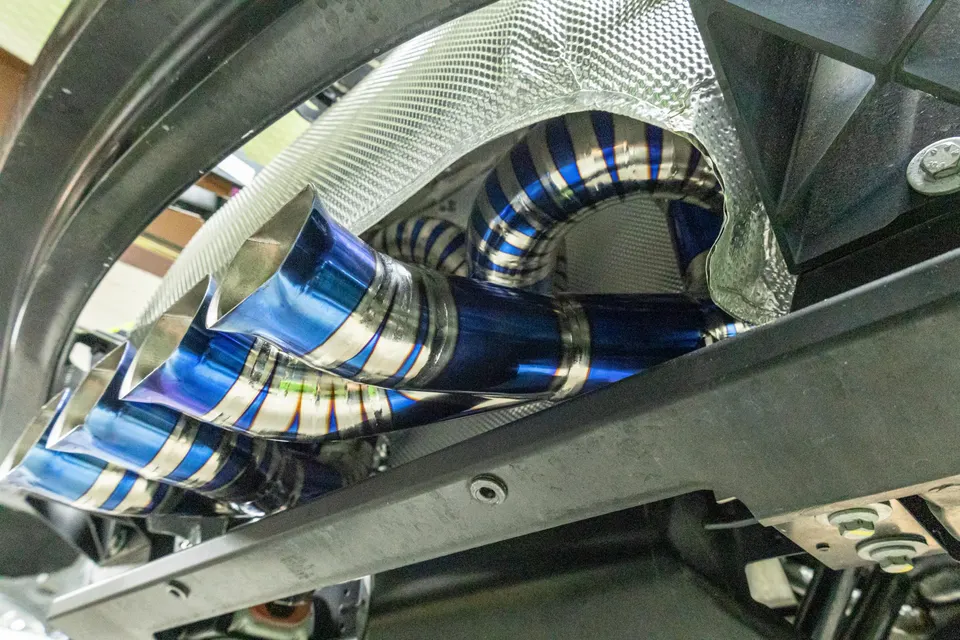 Close-up of a custom titanium exhaust system with blue tips and heat shielding installed under a performance car.