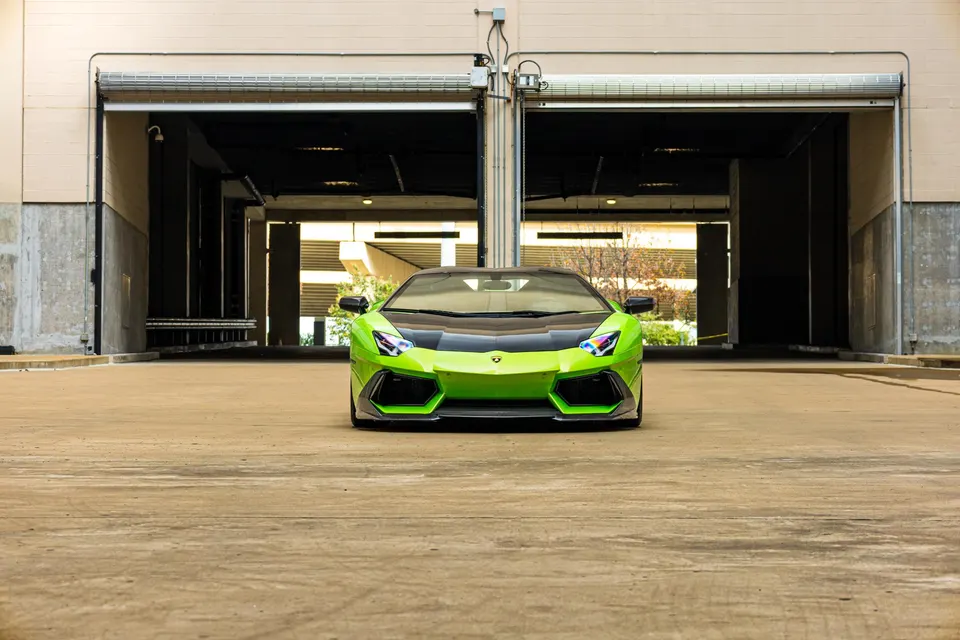 Front view of a vibrant green Lamborghini Aventador with a black hood, parked in front of two garage doors.