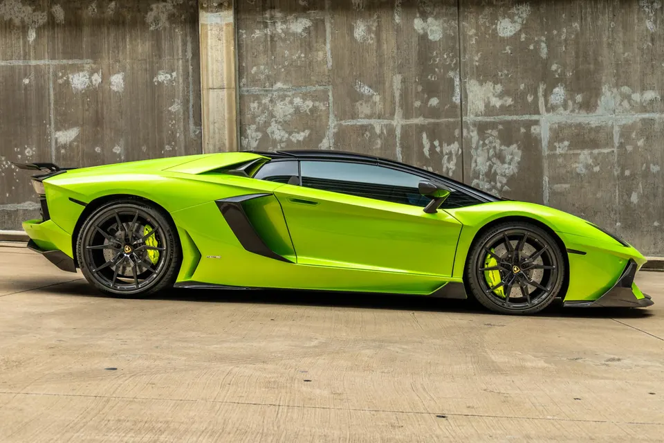 Lime green Lamborghini Aventador supercar with black wheels and yellow brake calipers parked against a concrete wall.