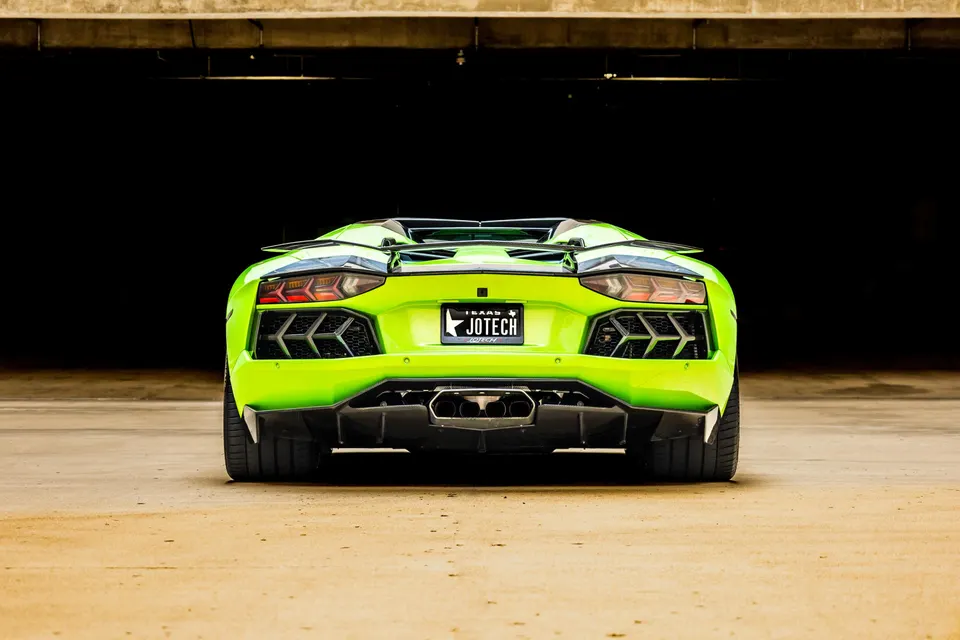 A lime green Lamborghini Aventador from the rear, showcasing its aggressive diffuser and exhaust tips in a parking garage.
