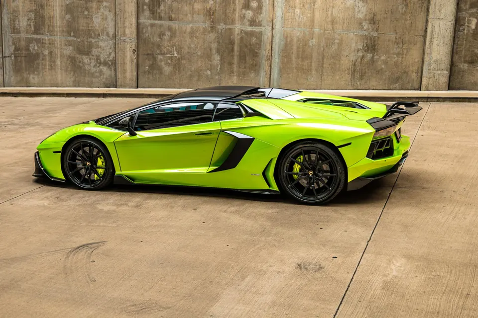 Lime green Lamborghini Aventador with a carbon fiber wing parked against a concrete wall.