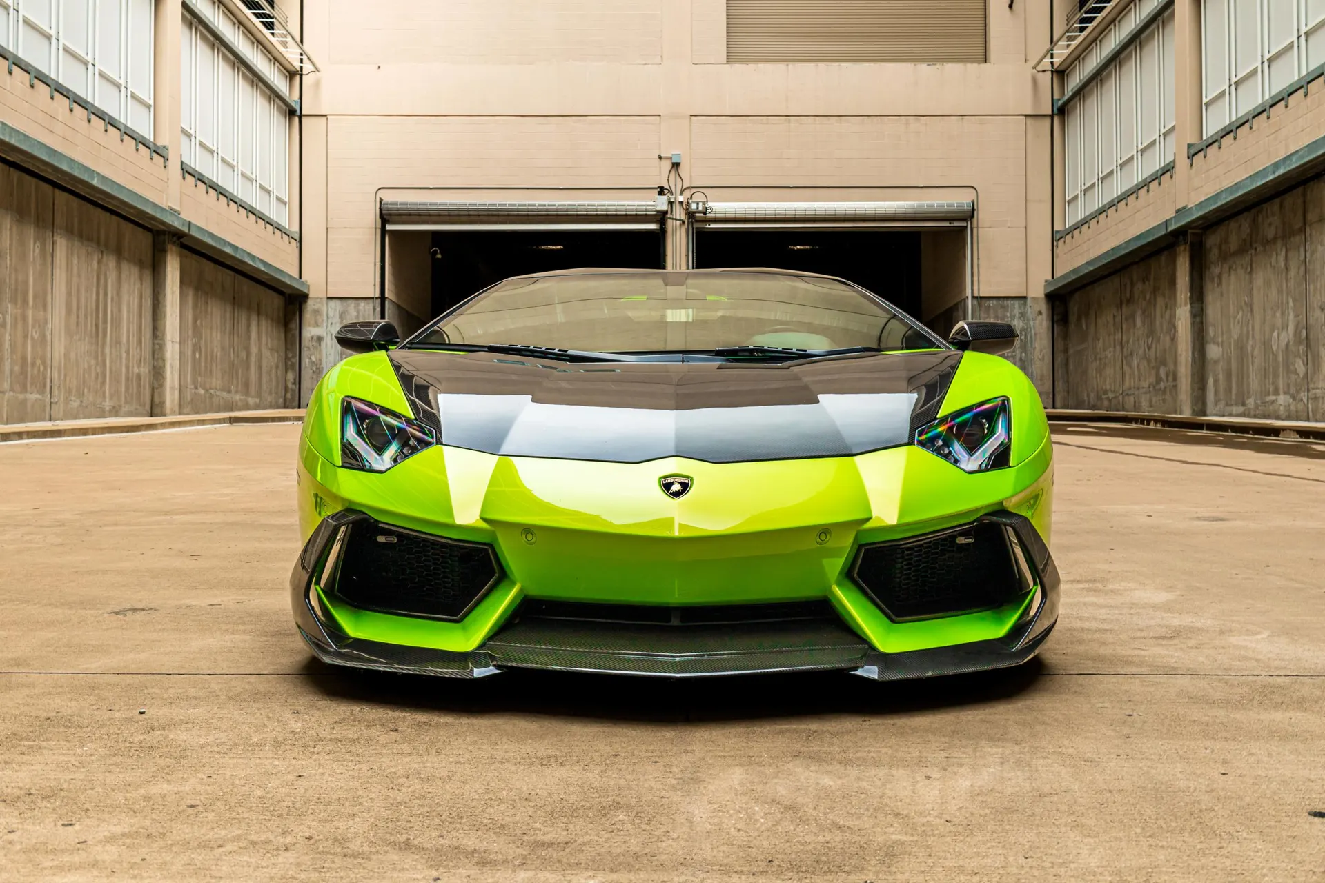 Front view of a vibrant lime green Lamborghini Aventador with a carbon fiber hood and splitter, parked in an industrial setting.