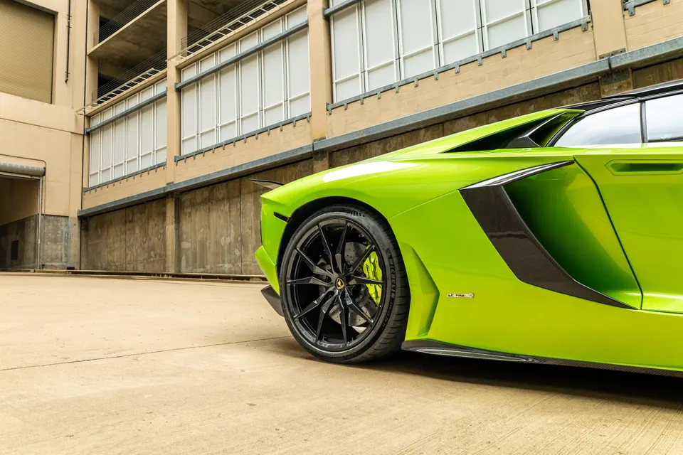 Lime green Lamborghini Aventador with black multi-spoke wheels and carbon fiber aero elements parked in a concrete structure.