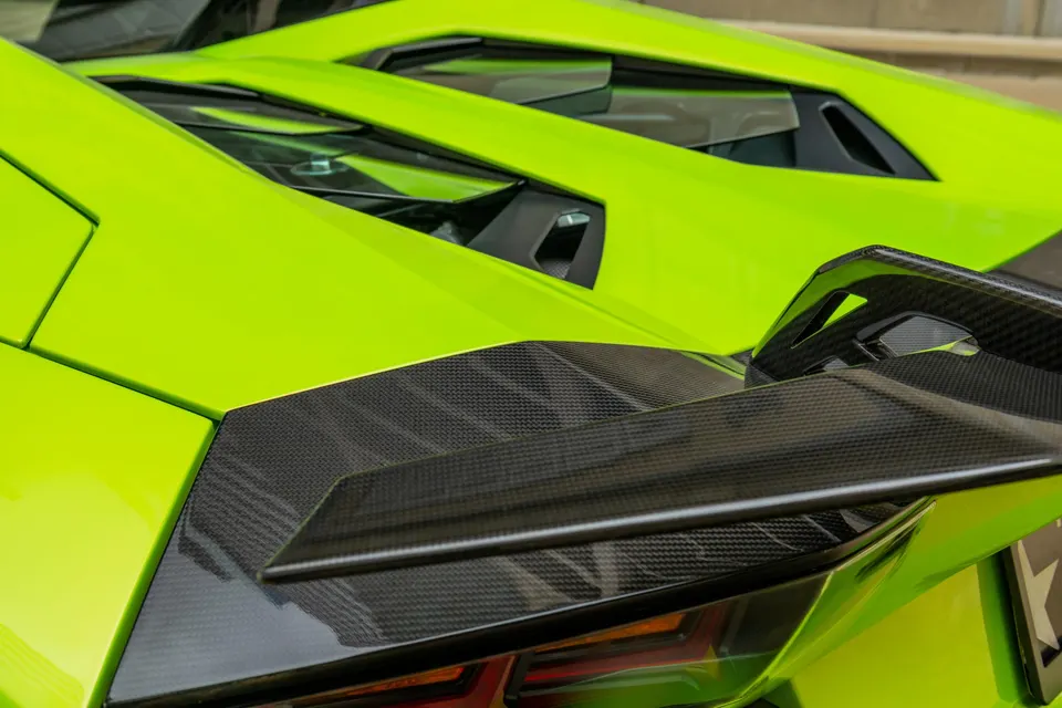 Close-up of a lime green Lamborghini Aventador's rear, highlighting the carbon fiber wing and engine cover.