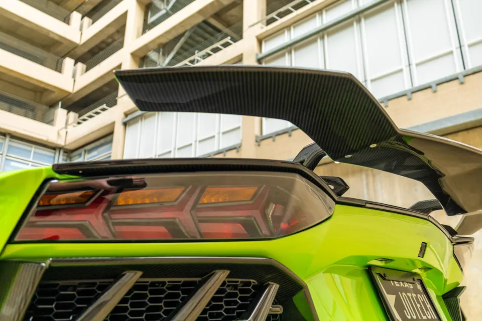 A lime green Lamborghini Aventador with a large carbon fiber rear wing and distinctive taillights.