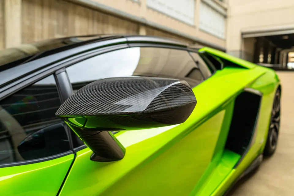 Close-up of a lime green Lamborghini's carbon fiber side mirror, showcasing the intricate weave and sleek design.