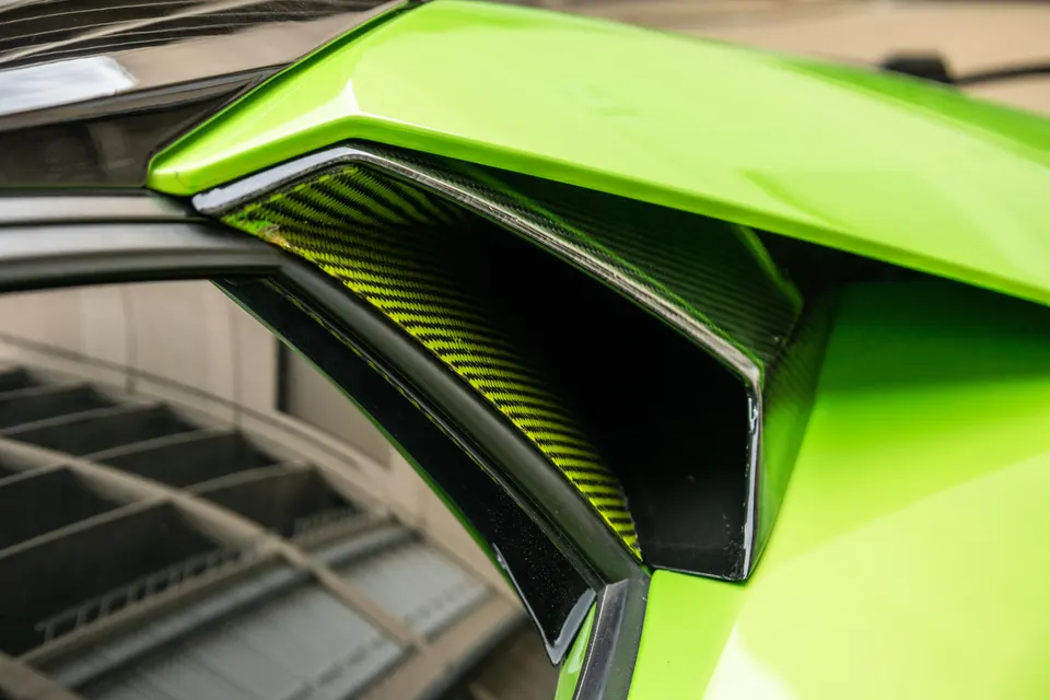 Close-up detail of a bright green Lamborghini's carbon fiber exterior vent, showcasing the texture and color.