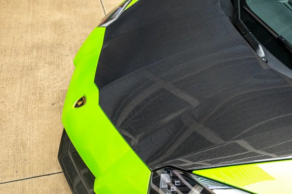 Close-up detail shot of a bright green Lamborghini's carbon fiber hood with the emblem.