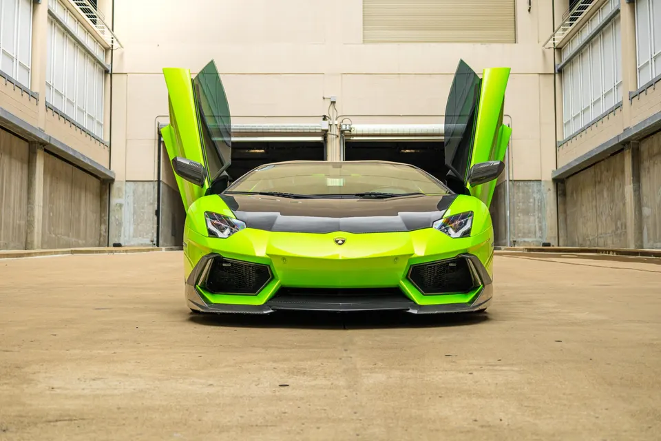 Lime green Lamborghini Aventador with scissor doors open, parked in a modern building setting.