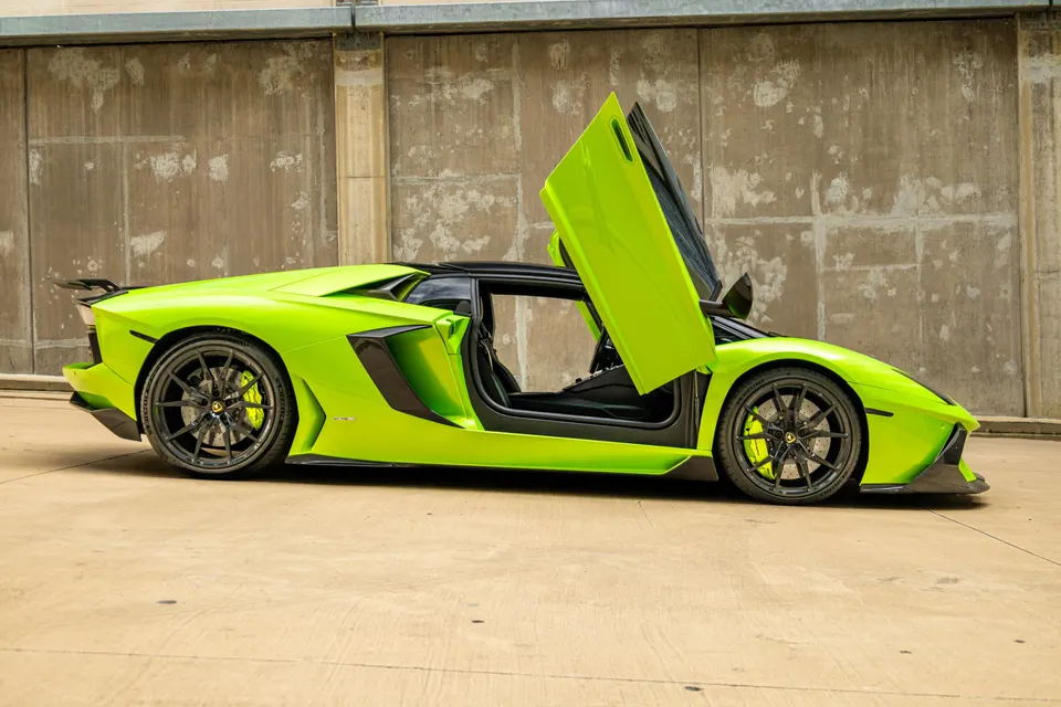 A lime green Lamborghini Aventador with its scissor doors open, parked in front of a concrete wall.