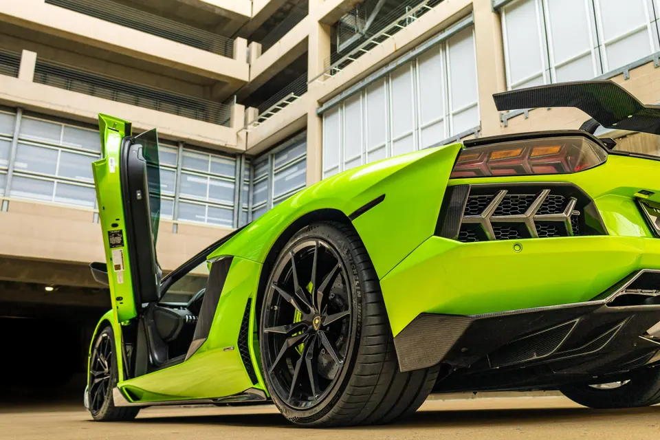 Lime green Lamborghini Aventador with carbon fiber rear wing and diffuser, custom black wheels, parked in a modern garage.