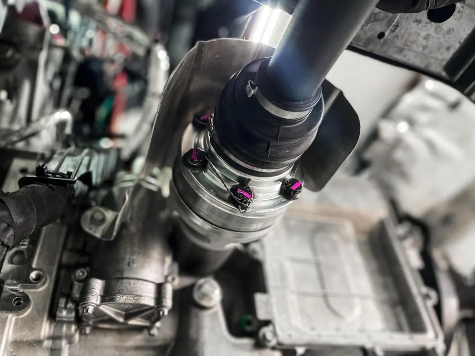 Close-up view of an aftermarket driveshaft or axle installed in a high-performance car's drivetrain with pink bolts.
