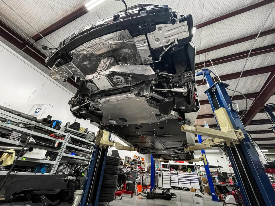 Underside view of a performance car on a lift in a Jotech Motorsports shop, showing suspension and chassis components.