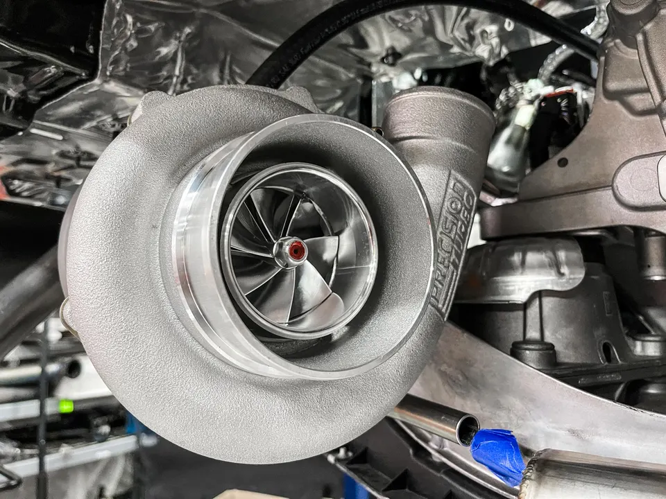 Close-up of a Precision Turbo turbocharger installed in an engine bay, showcasing the compressor wheel.