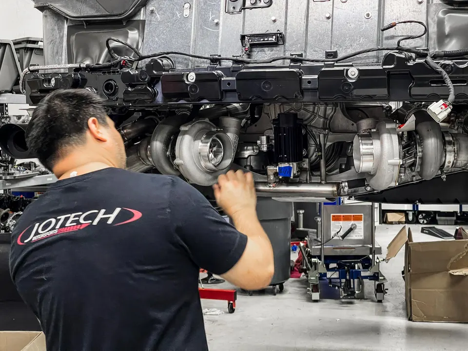 A Jotech Motorsports mechanic installs multiple turbochargers on a high-performance engine in a shop setting.