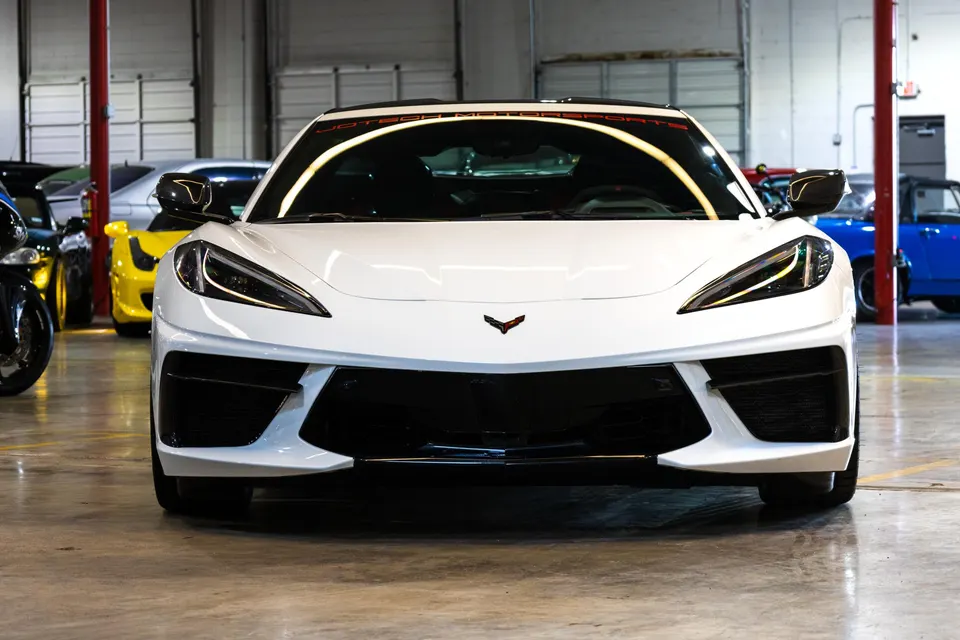 Front view of a white Chevrolet Corvette C8 parked in a clean garage or showroom, showcasing its sleek design.