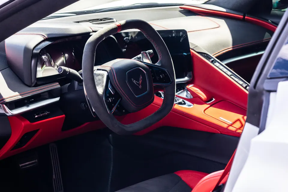 A detailed view of the red and black interior of a Chevrolet Corvette C8, showing the steering wheel and dashboard.