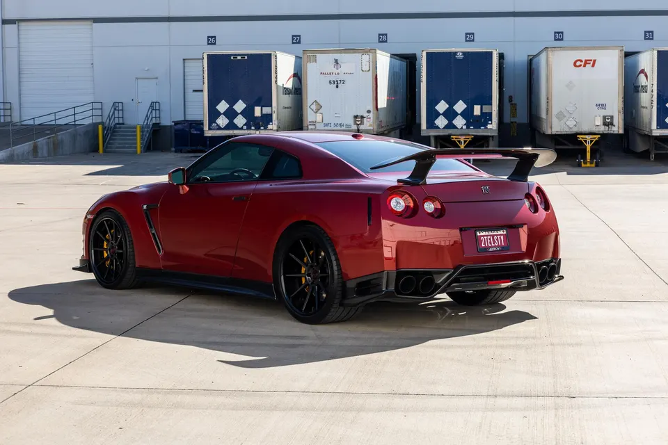 Red Nissan GT-R with aftermarket rear wing and diffuser parked in front of a loading dock.