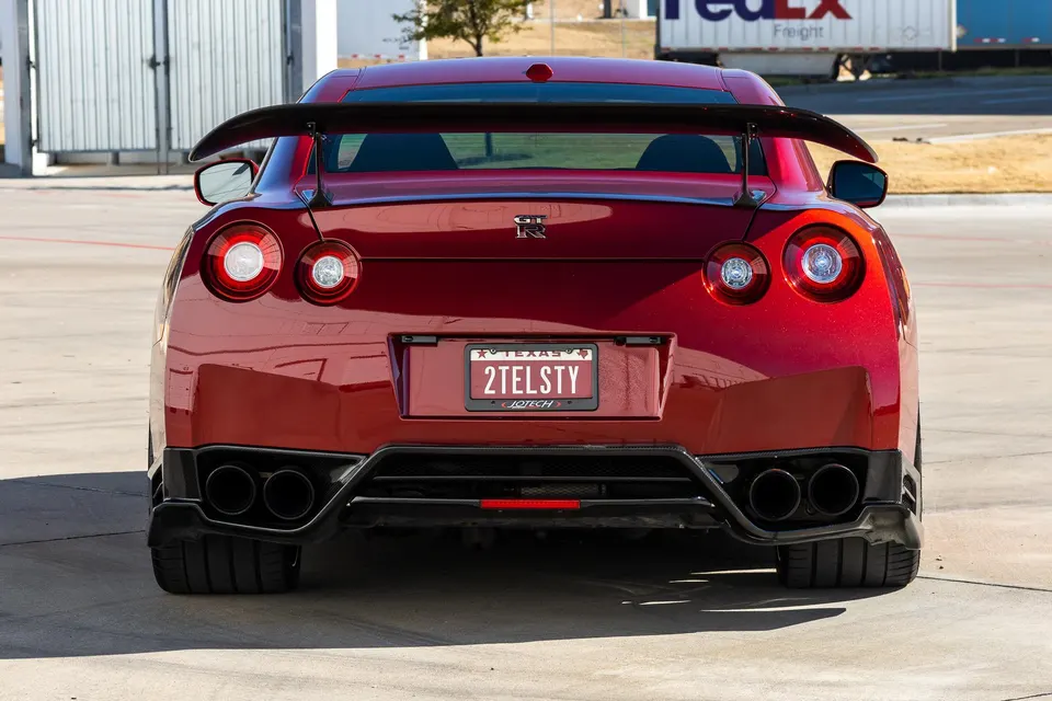 Rear view of a red Nissan GT-R with an aftermarket wing, quad exhaust, and diffuser parked outdoors.