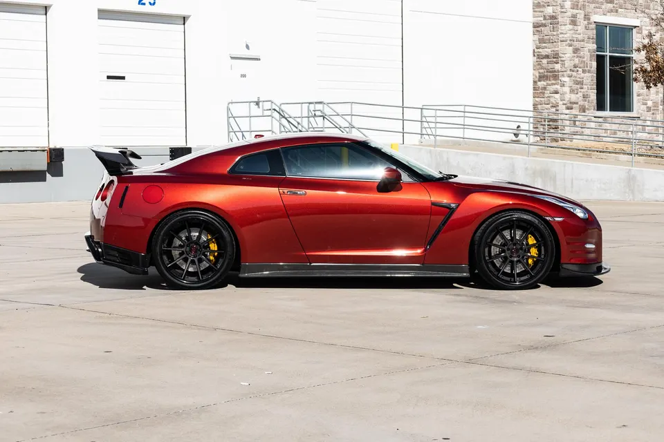A red Nissan GT-R with aftermarket wheels and a carbon fiber rear wing parked outside a commercial building.