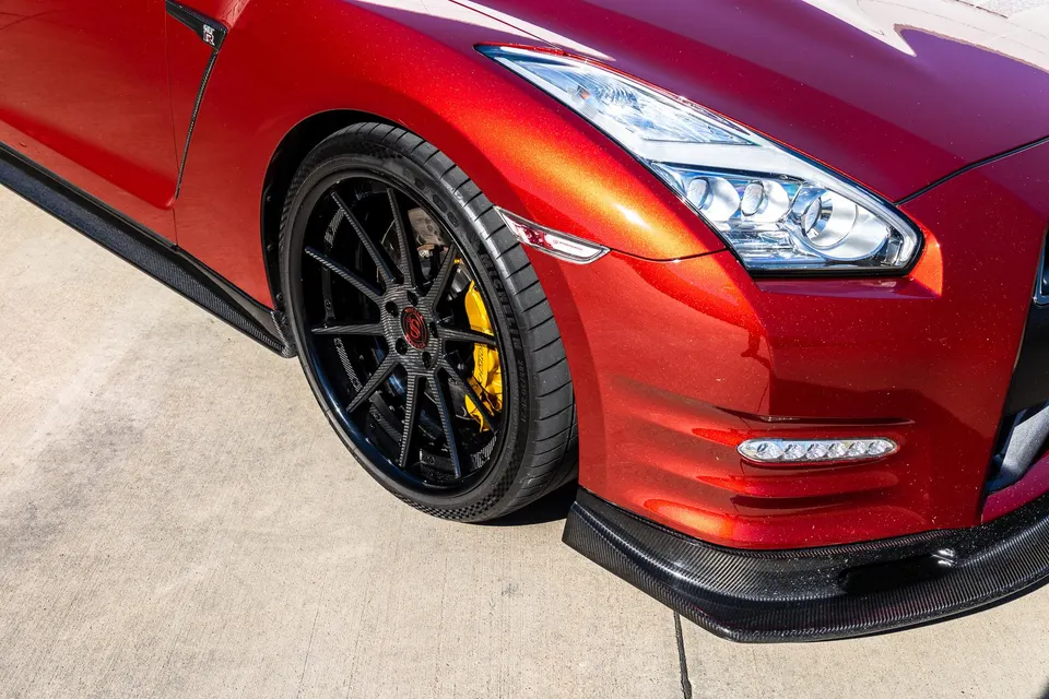 Close-up of a red Nissan GT-R's front with carbon fiber front splitter and side skirt, custom wheels, and yellow brake calipers.