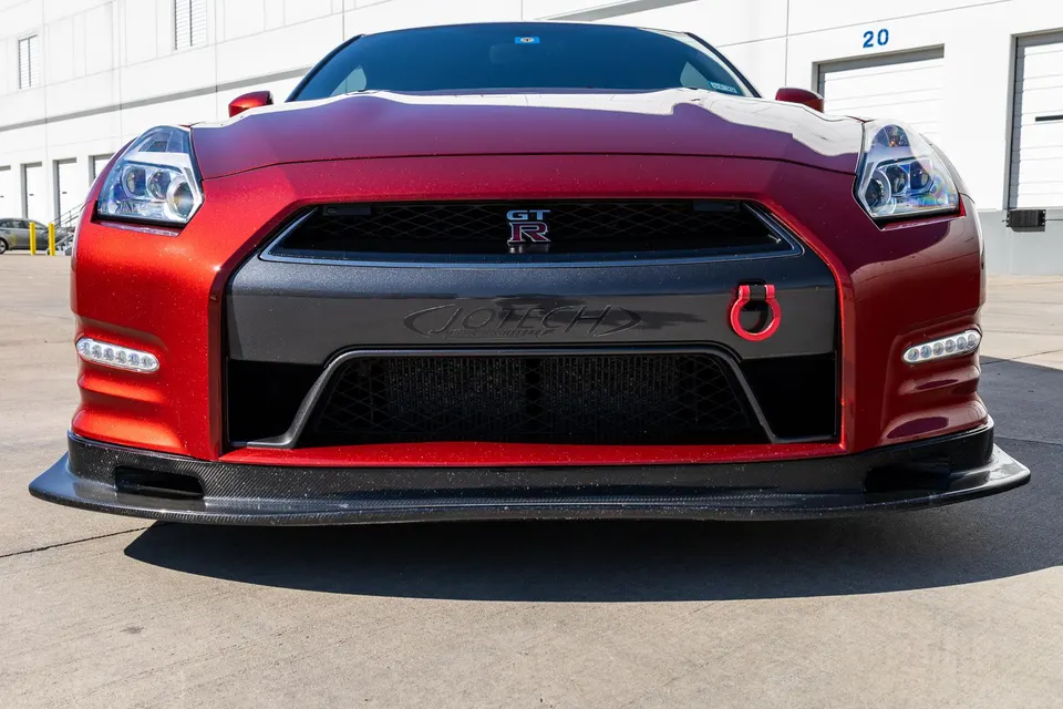 Front view of a red Nissan GT-R with a carbon fiber splitter and Jotech branding, parked outdoors.