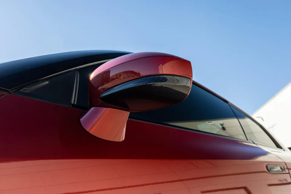 A close-up of the red car's side mirror and window, showcasing the exterior detail under a clear blue sky.