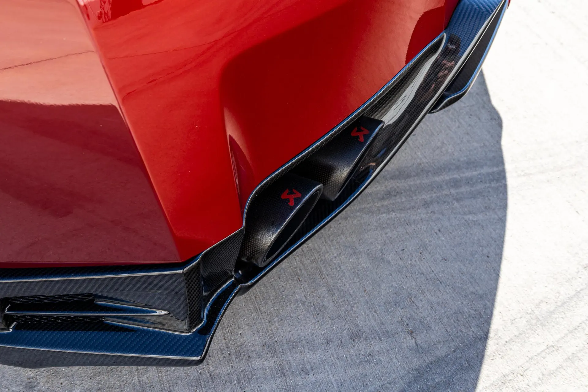 Close-up of a red car's carbon fiber rear diffuser and Akrapovic exhaust tips.