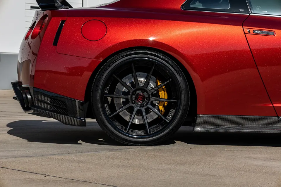 Close-up of a red Nissan GT-R's rear quarter panel, showcasing custom black wheels, yellow brake calipers, and carbon fiber aero.